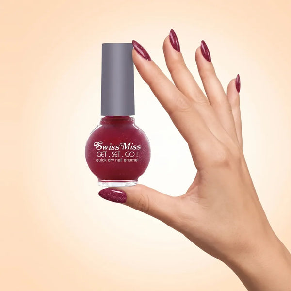 Swiss Miss Get Set Go Quick Dry Nail Enamel in shade Cherry Charisma F-409 held by hand showing round glass bottle with sparkling glittery deep cherry red polish and matching manicured nails.