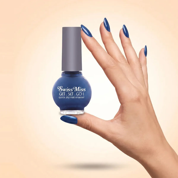 Swiss Miss Get Set Go Quick Dry Nail Enamel in shade Cobalt Craze F-407 held by hand showing round glass bottle with rich glossy cobalt blue polish and matching manicured nails.