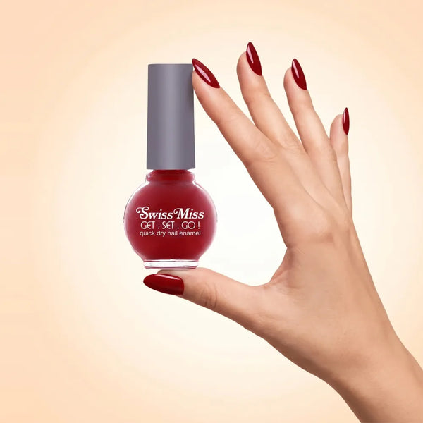 Swiss Miss Get Set Go Quick Dry Nail Enamel in shade Gypsy Rose 222 held by hand showing round glass bottle with rich crimson ruby red polish and matching manicured nails.