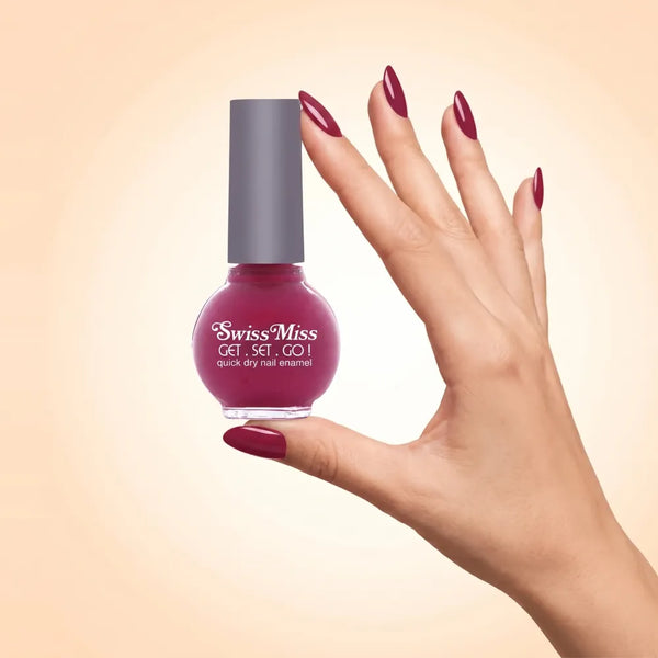 Swiss Miss Get Set Go Quick Dry Nail Enamel in shade Hot Hibiscus F-410 held by hand showing round glass bottle with smooth glossy vibrant magenta pink red polish and matching manicured nails.