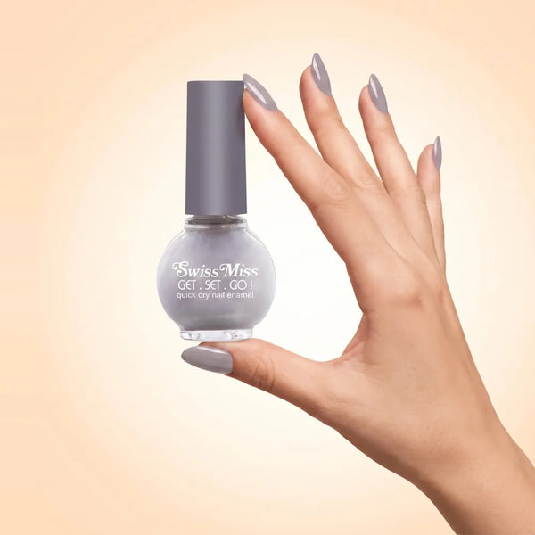 Swiss Miss Get Set Go Quick Dry Nail Enamel in shade Lilac Grey 802 held by hand showing round glass bottle with smooth soft lilac grey polish and matching manicured nails.