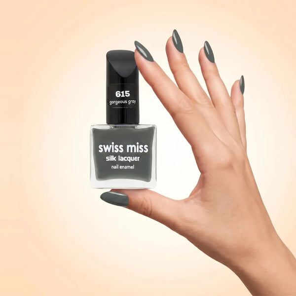 Swiss Miss Silk Lacquer Nail Enamel in shade Gorgeous Grey 615 held by hand showing clear glass square bottle with sleek slate grey polish and matching manicured nails.