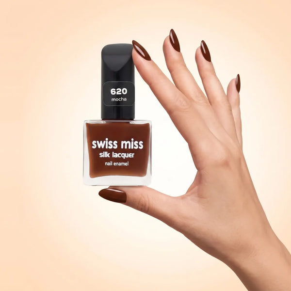 Swiss Miss Silk Lacquer Nail Enamel in shade Mocha 620 held by hand showing clear glass square bottle with rich mocha brown polish and matching manicured nails.