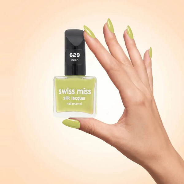 Swiss Miss Silk Lacquer Nail Enamel in shade Neon 629 held by hand showing clear glass square bottle with vibrant neon chartreuse lime green polish and matching manicured nails.