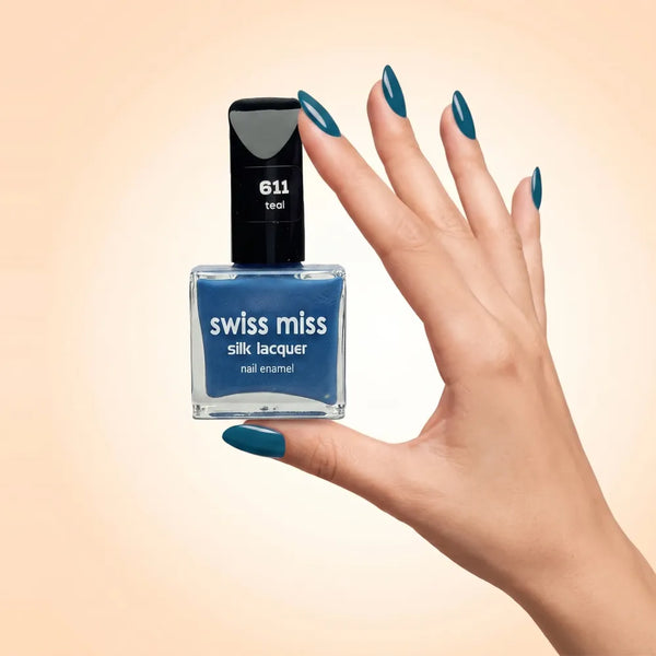 Swiss Miss Silk Lacquer Nail Enamel in shade Teal 611 held by hand showing clear glass square bottle with vibrant deep teal blue polish and matching manicured nails.