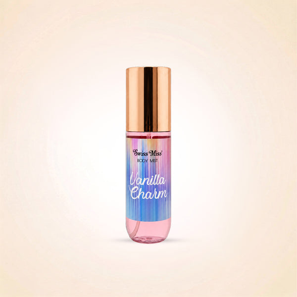 A body mist bottle with pump by Swiss Miss, labeled 'Vanilla Charm', featuring a metallic rose gold cap and a body of liquid with a vertical rainbow gradient of pink, purple, blue, and green, set against a soft beige background.