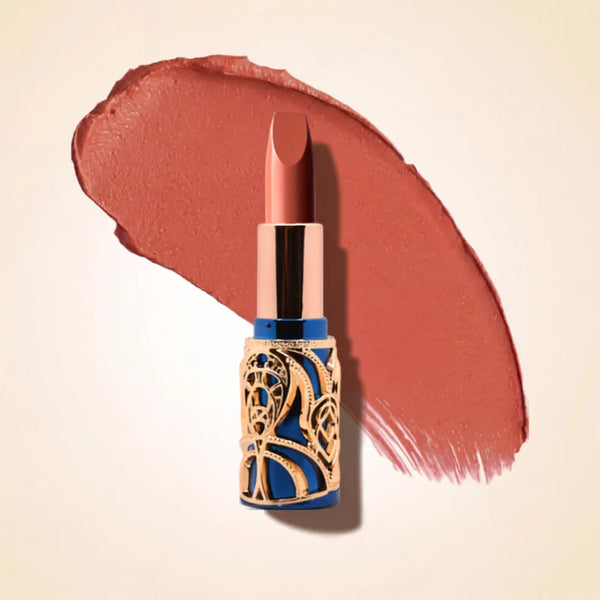 Swiss Miss Bling Lipstick in shade Nude Pink B-103 featuring ornate blue and gold filigree bullet tube casing with a warm peachy nude pink lipstick swatch.