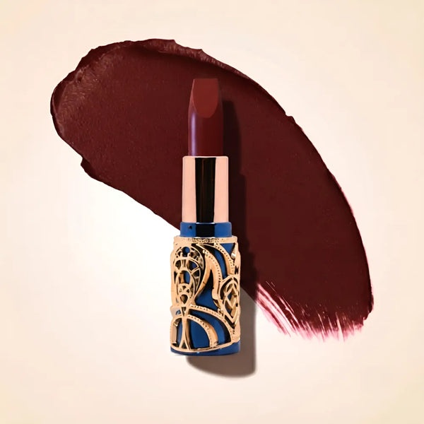 Swiss Miss Bling Lipstick in shade Rich Mood B-107 featuring ornate blue and gold filigree bullet tube casing with a deep moody dark burgundy brown lipstick swatch.