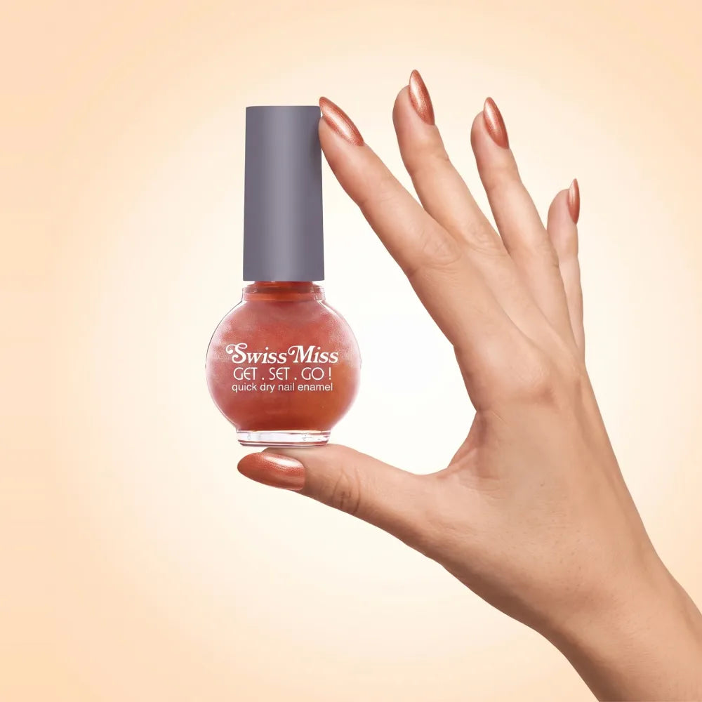 Swiss Miss Get Set Go Quick Dry Nail Enamel in shade Autumn Blaze F-408 held by hand showing round glass bottle with shimmering metallic warm burnt orange copper polish and matching manicured nails.