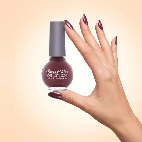 Swiss Miss Get Set Go Quick Dry Nail Enamel in shade Blossom Pink 247 held by hand showing round glass bottle with shimmering metallic deep berry plum pink polish and matching manicured nails.
