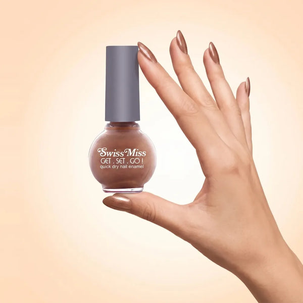 Swiss Miss Get Set Go Quick Dry Nail Enamel in shade Gold Dust 291 held by hand showing round glass bottle with shimmering metallic champagne gold bronze polish and matching manicured nails.