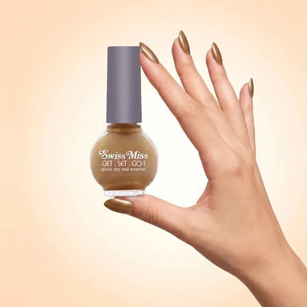 Swiss Miss Get Set Go Quick Dry Nail Enamel in shade Golden Hour F-404 held by hand showing round glass bottle with shimmering metallic warm golden bronze polish and matching manicured nails.