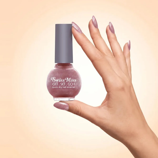 Swiss Miss Get Set Go Quick Dry Nail Enamel in shade Lilac Sizzle 250 held by hand showing round glass bottle with shimmering metallic lilac mauve pink polish and matching manicured nails.