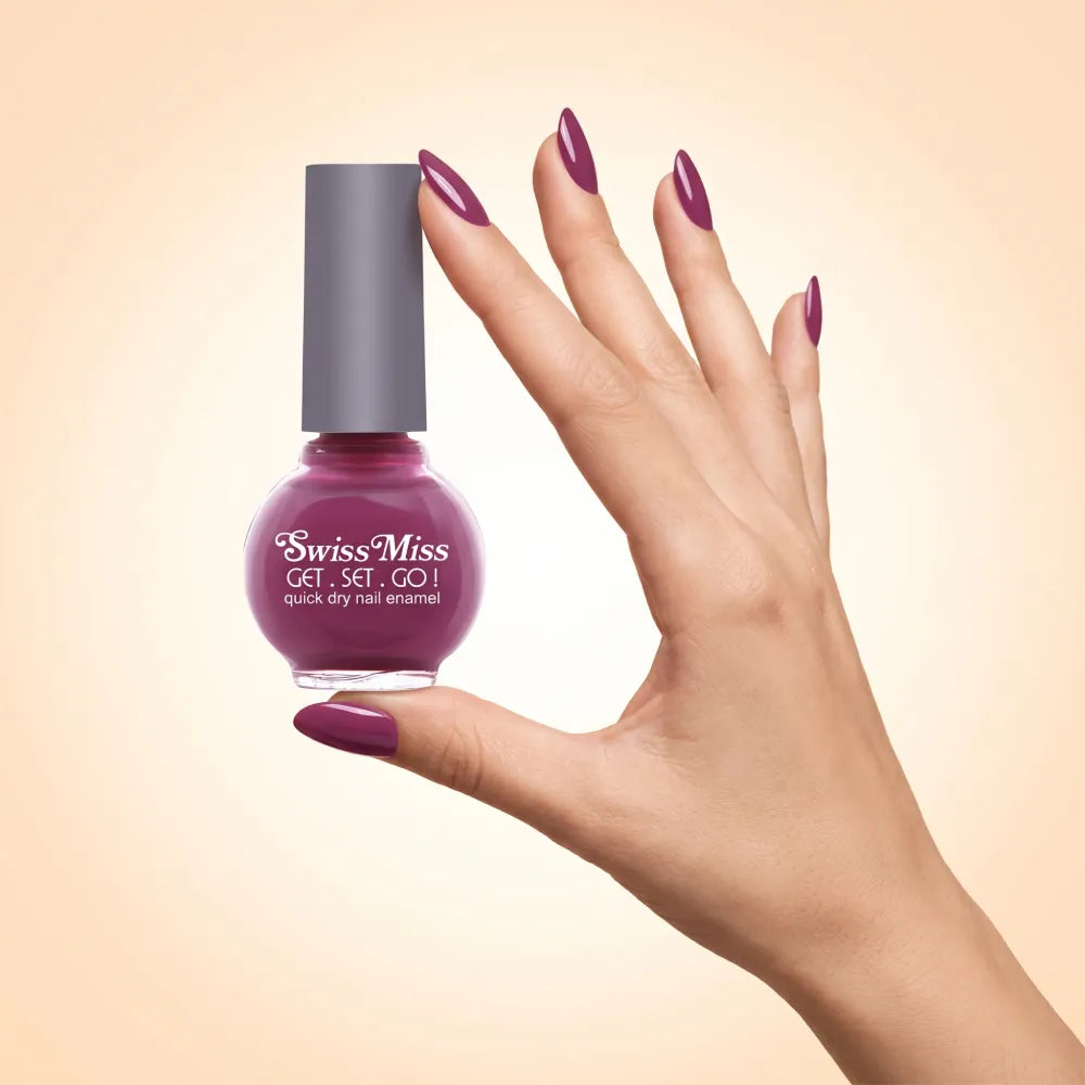 Swiss Miss Get Set Go Quick Dry Nail Enamel in shade Raspberry Rose 257 held by hand showing round glass bottle with rich raspberry plum rose polish and matching manicured nails.