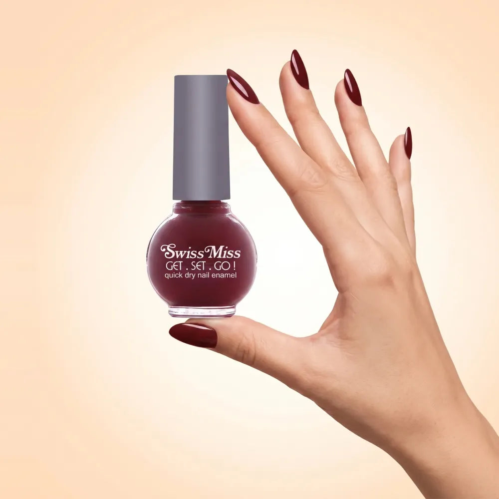 Swiss Miss Get Set Go Quick Dry Nail Enamel in shade Ribbon Red 224 held by hand showing round glass bottle with deep maroon ribbon red polish and matching manicured nails.