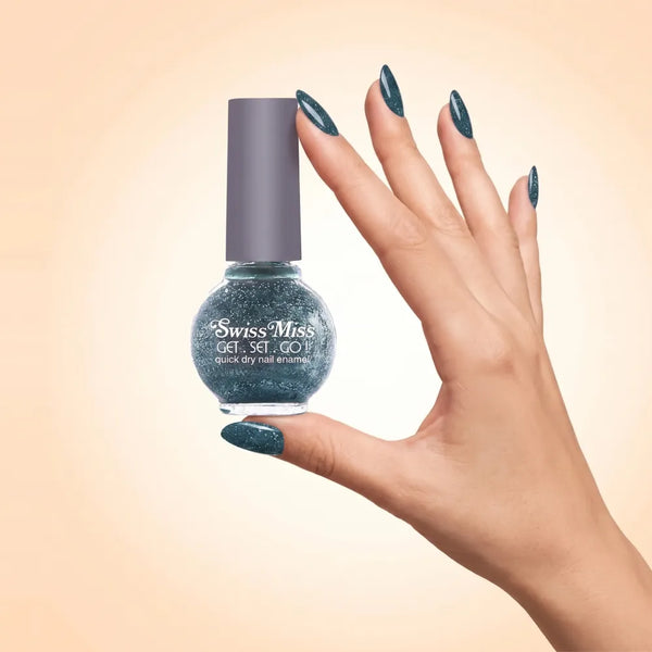 Swiss Miss Get Set Go Quick Dry Nail Enamel in shade Sapphire Sparkle F-401 held by hand showing round glass bottle with sparkling glittery deep sapphire teal blue polish and matching manicured nails.