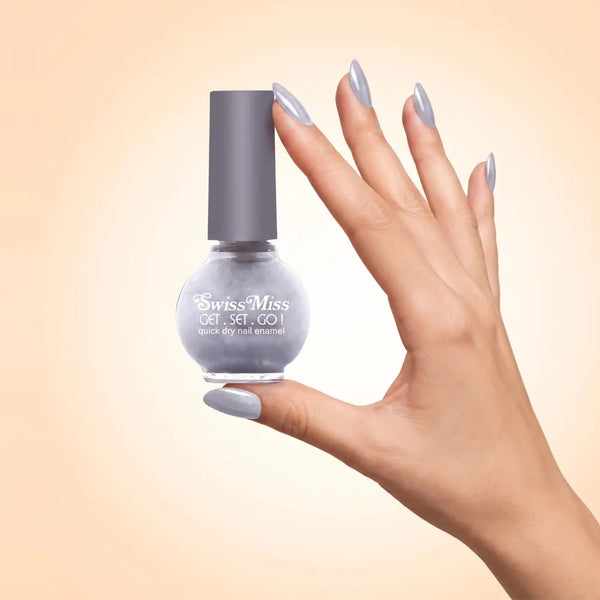 Swiss Miss Get Set Go Quick Dry Nail Enamel in shade Silver Lining 812 held by hand showing round glass bottle with shimmering metallic light silver grey polish and matching manicured nails.