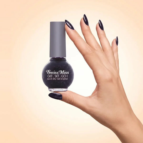 Swiss Miss Get Set Go Quick Dry Nail Enamel in shade Starlit Night F-403 held by hand showing round glass bottle with sparkling glittery deep dark navy black polish and matching manicured nails.