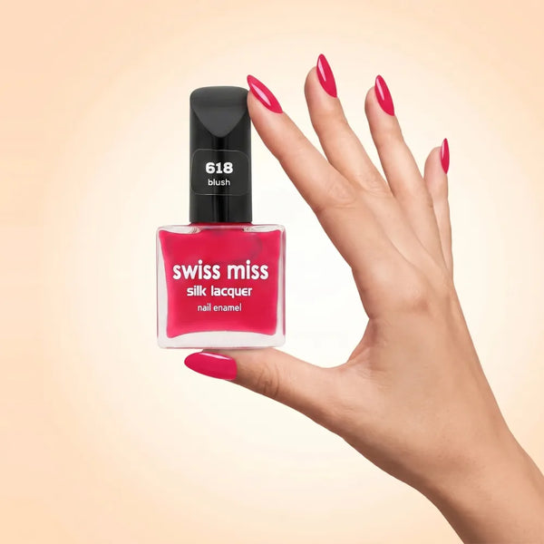 Swiss Miss Silk Lacquer Nail Enamel in shade Blush 618 held by hand showing clear glass square bottle with vibrant magenta hot pink polish and matching manicured nails.