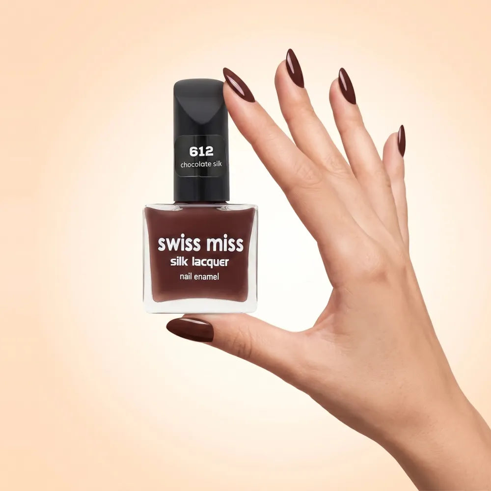 Swiss Miss Silk Lacquer Nail Enamel in shade Chocolate Silk 612 held by hand showing clear glass square bottle with deep warm chocolate brown polish and matching manicured nails.
