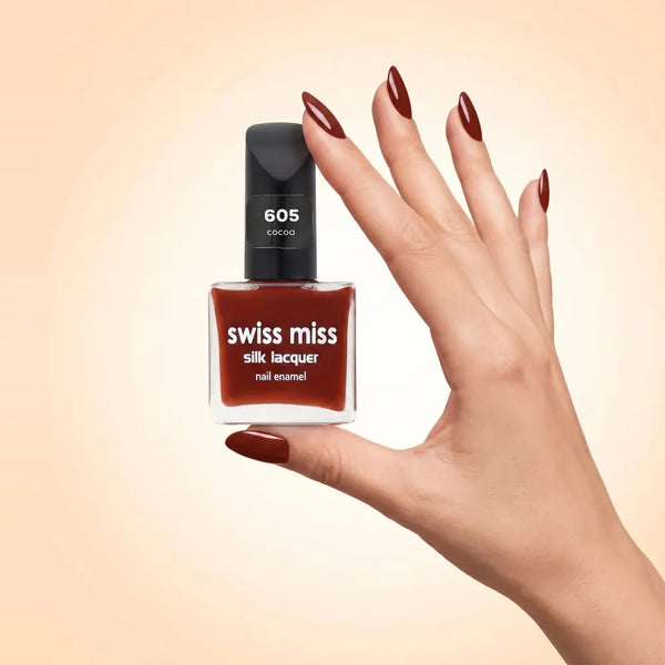 Swiss Miss Silk Lacquer Nail Enamel in shade Cocoa 605 held by hand showing clear glass square bottle with rich dark chocolate cocoa brown polish and matching manicured nails.
