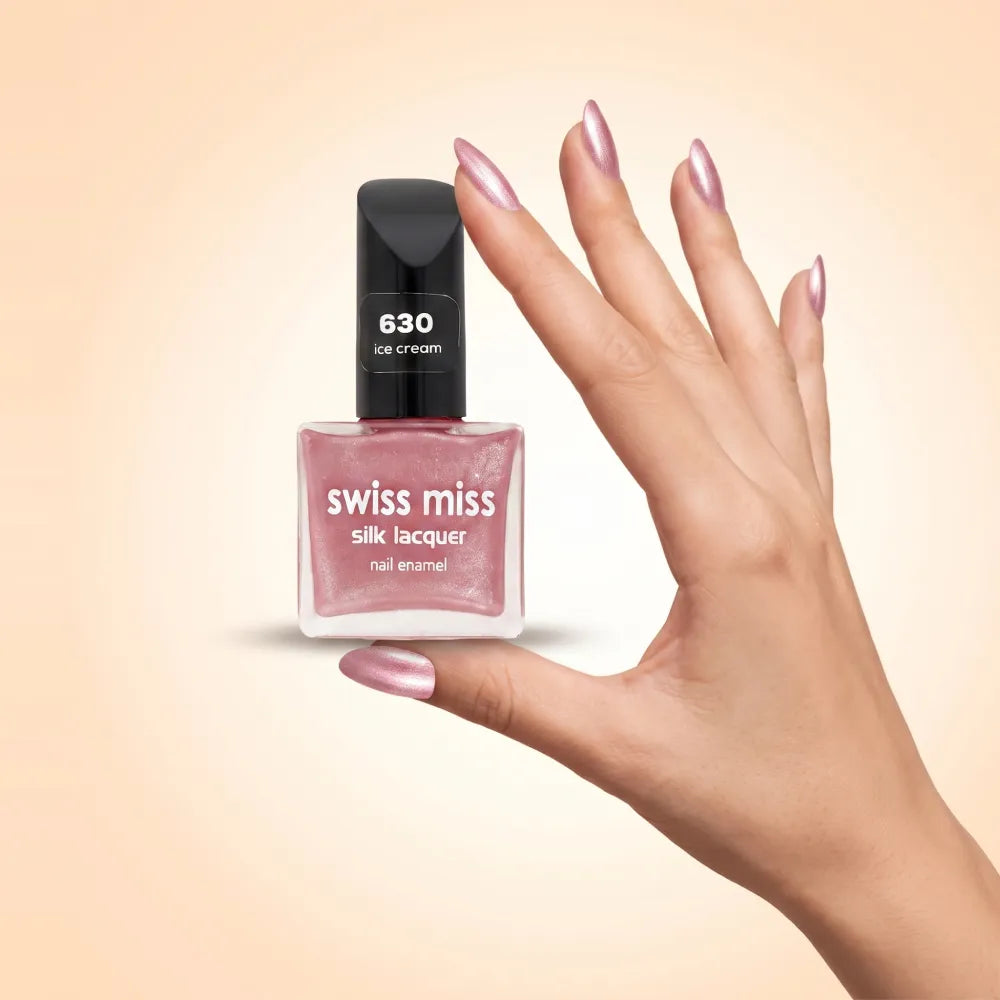 Swiss Miss Silk Lacquer Nail Enamel in shade Ice Cream 630 held by hand showing clear glass square bottle with shimmering metallic light pink polish and matching manicured nails.