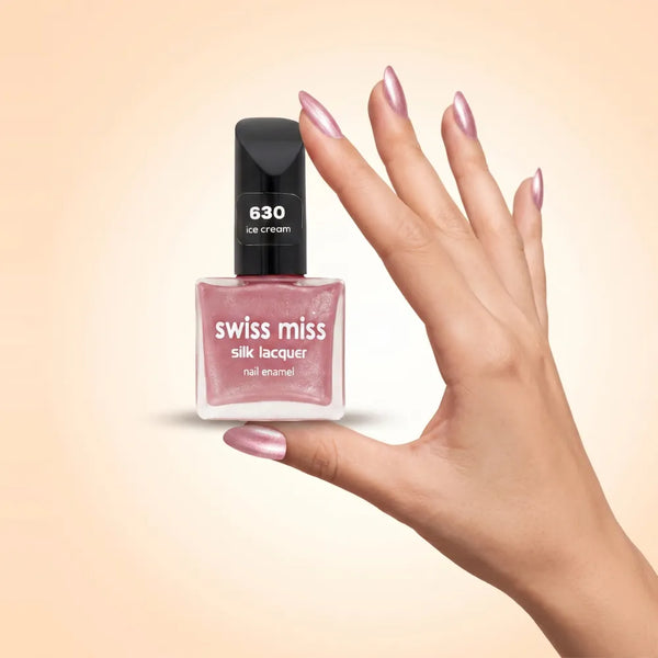 Swiss Miss Silk Lacquer Nail Enamel in shade Ice Cream 630 held by hand showing clear glass square bottle with shimmering metallic light pink polish and matching manicured nails.