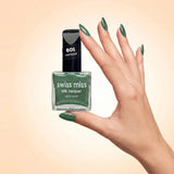 Swiss Miss Silk Lacquer Nail Enamel in shade Mermaid 601 held by hand showing clear glass square bottle with metallic emerald green polish and matching manicured nails.