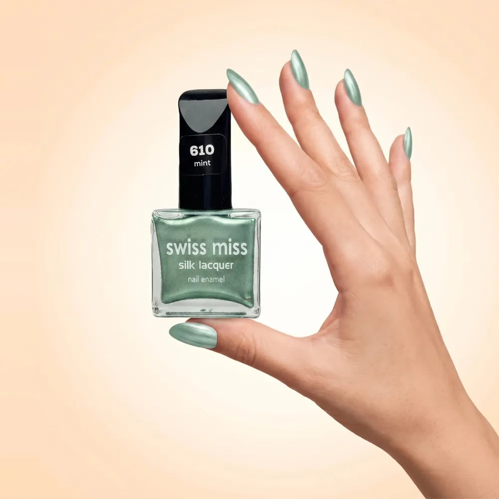 Swiss Miss Silk Lacquer Nail Enamel in shade Mint 610 held by hand showing clear glass square bottle with metallic shimmer light mint green polish and matching manicured nails.