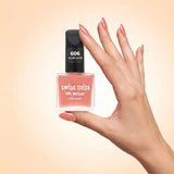 Swiss Miss Silk Lacquer Nail Enamel in shade Nude Pink 606 held by hand showing clear glass square bottle with soft peachy nude pink polish and matching manicured nails.