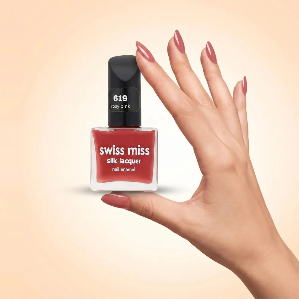 Swiss Miss Silk Lacquer Nail Enamel in shade Rosy Pink 619 held by hand showing clear glass square bottle with dusty rose pink polish and matching manicured nails.