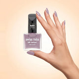 Swiss Miss Silk Lacquer Nail Enamel in shade Unicorn 623 held by hand showing clear glass square bottle with soft dusty lilac purple polish and matching manicured nails.