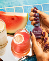 Woman holding Swiss Miss Get Set Go quick dry nail polish bottle in Blossom Pink 247 with a dark mauve plum manicure by a pool.