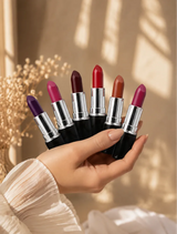 A hand holding six open Swiss Miss Classic Lipsticks displaying various shades against a warm aesthetic background.