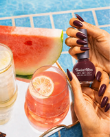 Woman holding Swiss Miss Get Set Go quick dry nail polish bottle in Dark Chocolate 223 with a matching deep brown manicure by a pool
