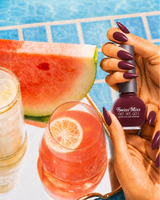Woman holding Swiss Miss Get Set Go quick dry nail polish bottle in Flamingo Pink 228 with a deep berry pink manicure by a pool.