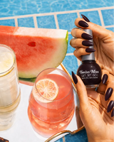Woman holding Swiss Miss Get Set Go quick dry nail polish bottle in Satin 214 with a dark purple black manicure by a pool.