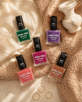 Aesthetic flat lay arrangement of five Swiss Miss Silk Lacquer nail polish bottles resting on cozy fabric and fleece with decorative gold rings and a small vase.
