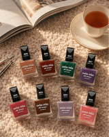 Flat lay arrangement of Swiss Miss Silk Lacquer nail polish bottles on a cozy carpet next to a teacup, open book, and manicure tools.