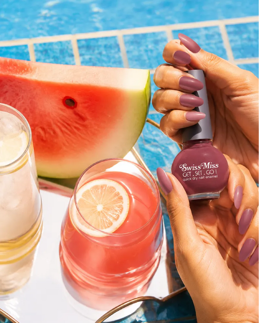 Woman holding Swiss Miss Get Set Go quick dry nail polish in Sugar Pink 209 with matching mauve pink manicure by a pool.