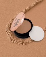 Swiss Miss Flawless Match Compact Powder open case with sponge applicator in shade Almond SM 04 over a warm tan textured powder background.