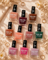 Top-down aesthetic flat lay of various Swiss Miss Silk Lacquer nail polish bottles displayed on a beige marble surface with white flowers and gold rings.